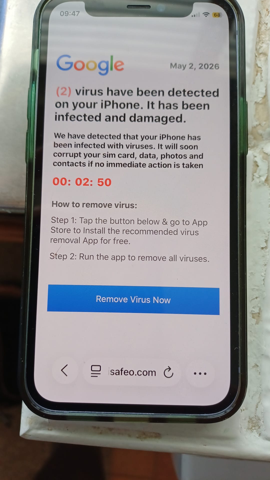 An iPhone sits on a surface displaying a web page. The page displays a Google logo and states that &lsquo;(2) virus have been detected on your iPhone. It has been infected and damaged.&rsquo;